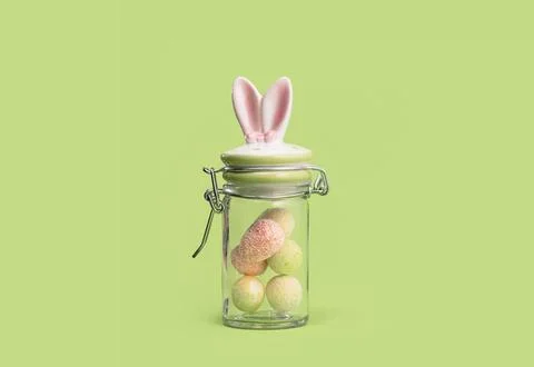 Easter bunny sweets jar with tiny eggs on green background. Stock Photos