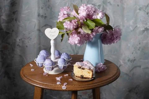 Easter cake and painted eggs and a bouquet of pink sakura flowers on a table Stock Photos