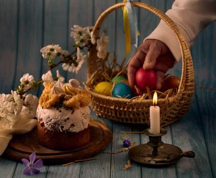 Easter cake, a basket with colored eggs, a bronze candlestick with a burning Stock Photos