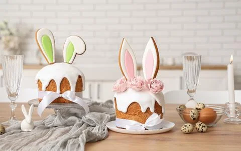 Easter cake with bunny ears, eggs and burning candle on table in kitchen Stock Photos