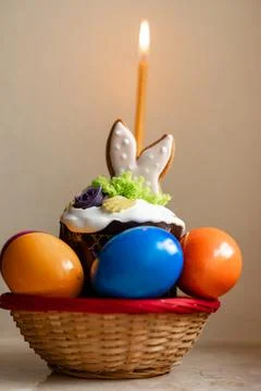Easter cake with a lit candle. Easter colorful eggs in a basket on the table Stock Photos