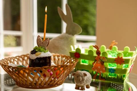 Easter cake with a lit candle. Easter colorful eggs in a basket on the table Stock Photos