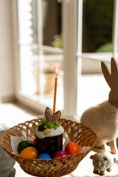 Easter cake with a lit candle. Easter colorful eggs in a basket on the table Stock Photos