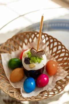 Easter cake with a lit candle. Easter colorful eggs in a basket on the table Stock Photos