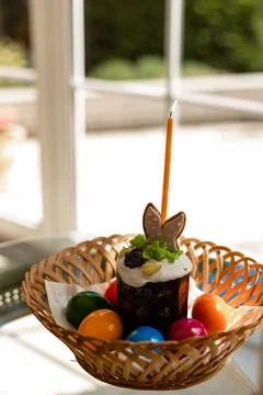 Easter cake with a lit candle. Easter colorful eggs in a basket on the table Stock Photos