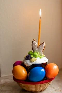 Easter cake with a lit candle. Easter colorful eggs in a basket on the table Stock Photos