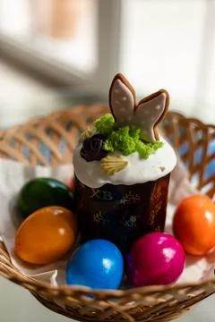 Easter cake with a lit candle. Easter colorful eggs in a basket on the table Stock Photos