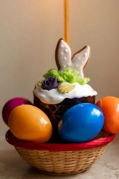 Easter cake with a lit candle. Easter colorful eggs in a basket on the table Stock Photos