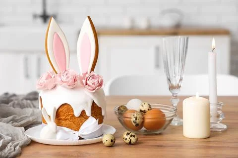 Easter cakes with bunny ears, eggs and burning candles on table in kitchen Stock Photos