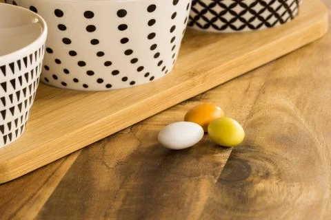 Easter candy eggs on wooden surface besides withe bowls with black pattern Foto stock