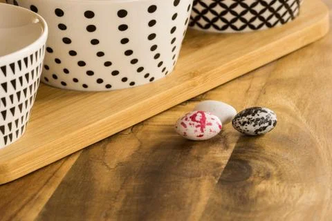 Easter candy eggs on wooden surface besides withe bowls with black pattern Stock-Fotos