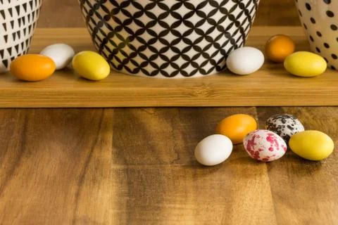 Easter candy eggs on wooden surface besides withe bowls with black pattern Foto stock