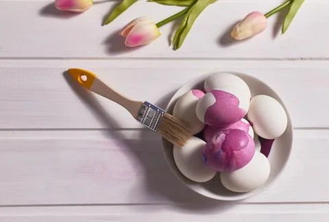 Easter card. Eggs, brush, paint, a bouquet of tulips on a white table. Stock Photos