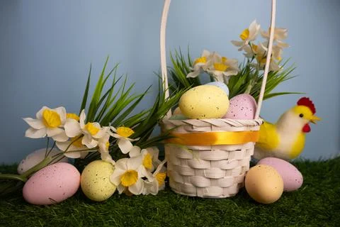Easter card featuring a white basket with pastel colorful eggs and daffodil f Stock Photos