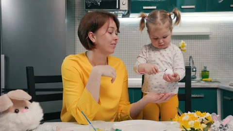 Easter celebration. Smiling mother teaching her toddler daughter painting eggs Stock Footage 219788251