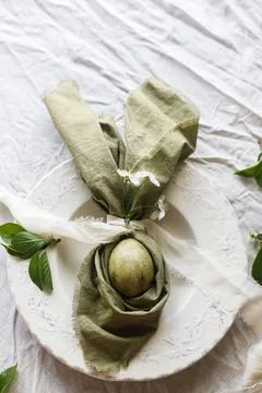 Easter celebration. Stylish green easter egg in linen bunny ears napkin wit.. 스톡 사진