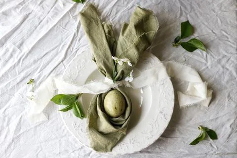Easter celebration. Stylish green easter egg in linen bunny ears napkin wit.. 库存照片