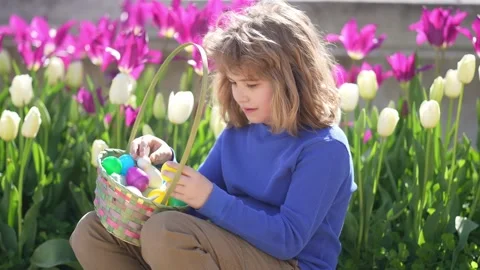 Easter child in blossom spring park. Kid hunting Easter eggs near tulips. Kid Stock Footage 320860179