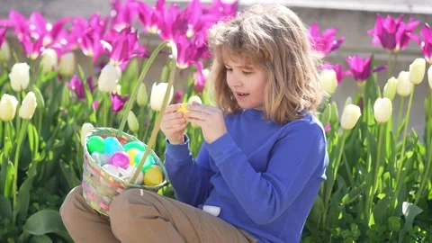 Easter child in blossom spring park. Kid hunting Easter eggs near tulips. Kid Stock Footage 321281863