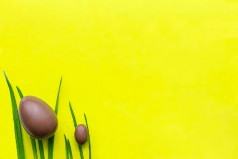 Easter chocolate eggs on the grass, big and small. Yellow background, green l Stock Photos