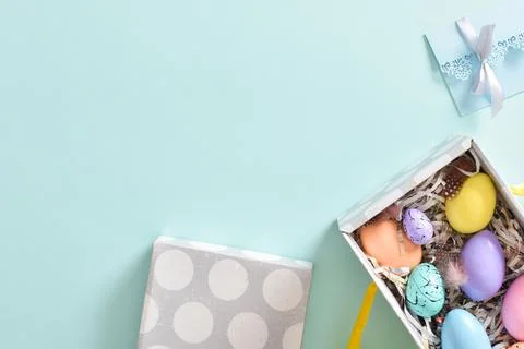 Easter colored eggs are in a box next to rabbit ears and a blue envelope. Ban Stock Photos