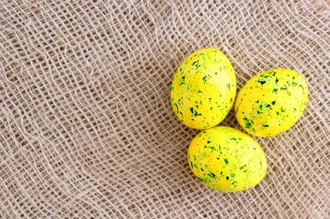 Easter colored eggs are yellow with green splashes. On linen brown fabric. Stock Photos