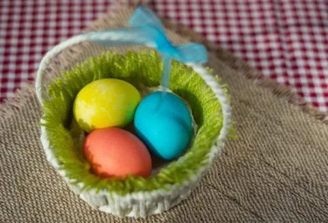 Easter colored eggs in a basket on a canvas napkin and checkered tablecloth. Stock Photos