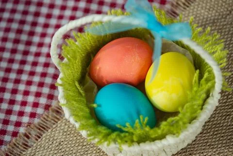 Easter colored eggs in a basket on a canvas napkin and checkered tablecloth. Stock Photos