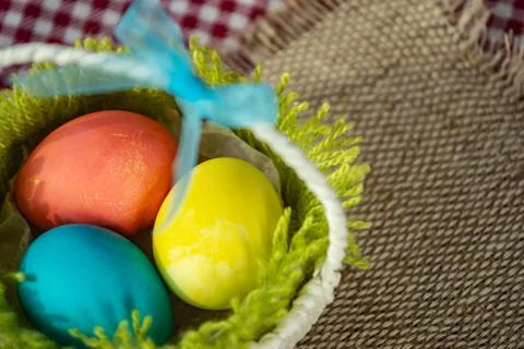 Easter colored eggs in a basket on a canvas napkin and checkered tablecloth. Stock Photos
