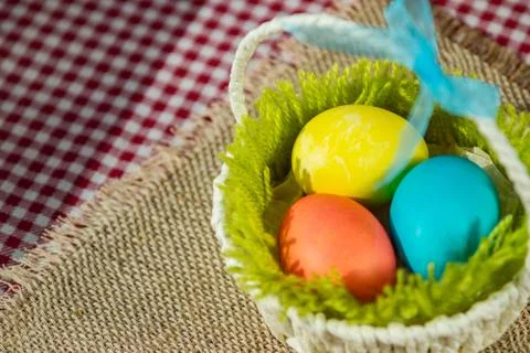 Easter colored eggs in a basket on a canvas napkin and checkered tablecloth. 写真素材