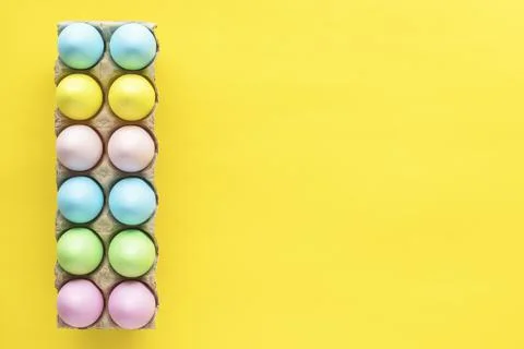 Easter colored eggs in egg carton on yellow background. Stock Photos