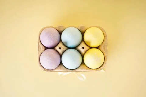 Easter colored eggs in egg tray on yellow background. Top view. Stock Photos