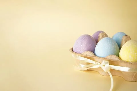 Easter colored eggs in egg tray on yellow background. Space for text. Stock Photos