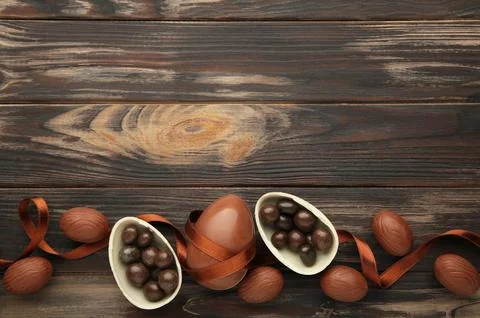 Easter composition with chocolate eggs and brown ribbon on brown wooden backg Stock Photos