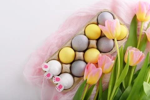 Easter composition of eggs, tulips and rabbit paws in cardboard box on white Stock Photos