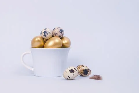 Easter composition of golden decorative and quail eggs in porcelain cup Stock Photos