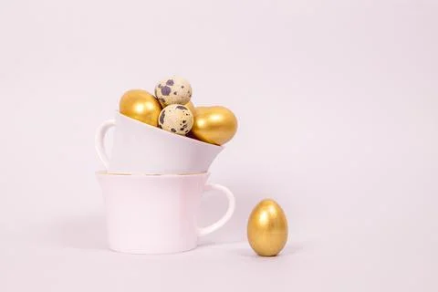 Easter composition of golden decorative and quail eggs in porcelain cups Stock Photos
