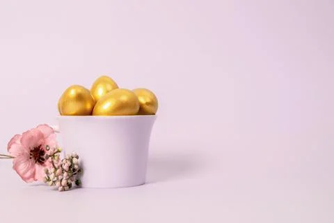 Easter composition of golden decorative eggs in a porcelain cup and a flower Stock Photos