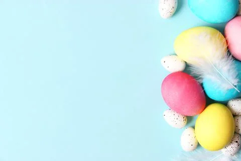 Easter composition of painted eggs and feathers on a colored background. 库存照片