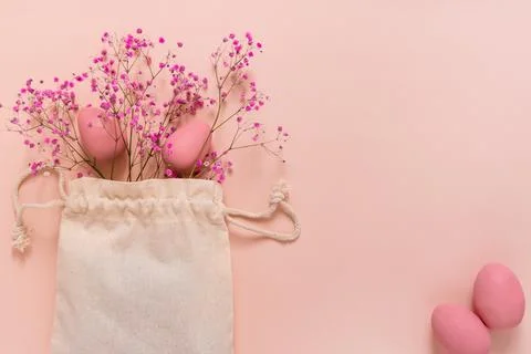 Easter composition with pink eggs and flowers arranged near bag Stock Photos