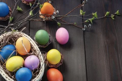 Easter composition - several colored eggs in a basket and on a dark wooden ta Stock Photos