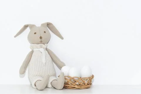 Easter composition with a soft rabbit toy and white eggs in a basket on a she Stock Photos