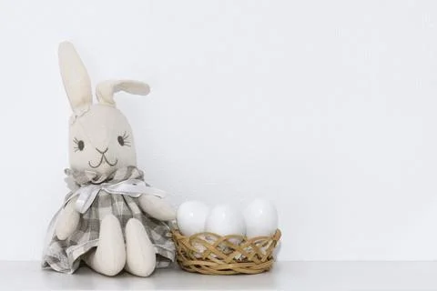 Easter composition with a soft rabbit toy and white eggs in a basket on a she Stock Photos