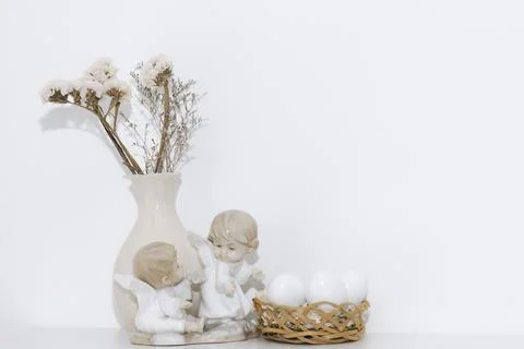 Easter composition with white eggs in a basket with sculptures of angels and  Stock Photos