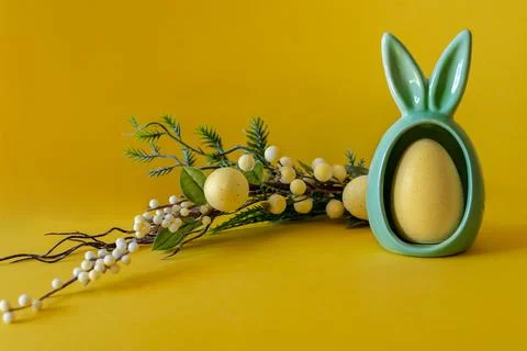 Easter composition on a yellow background. Egg with bunny ears and a branch a Stock Photos