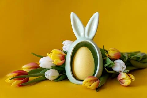 Easter concept. Egg with rabbit ears and tulips on a yellow background with s Stock Photos