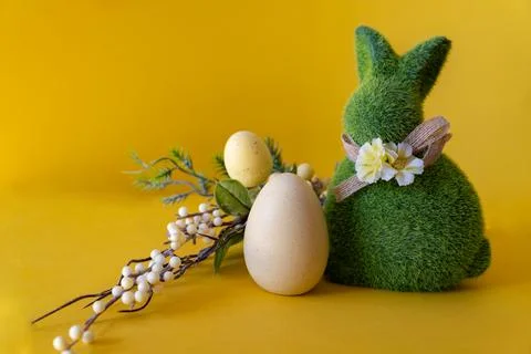 Easter concept. Green Easter bunny with a branch with Easter eggs on a yellow Stock Photos