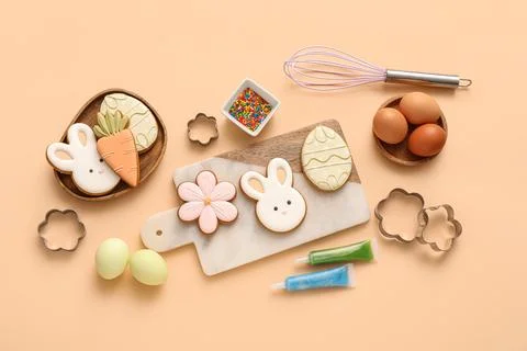 Easter cookies with eggs, icing tubes and kitchen utensils on beige backgroun Stock Photos