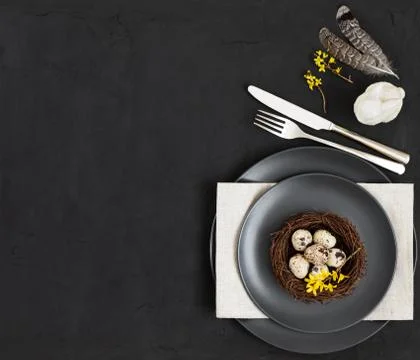 Easter dark table setting with a nest of quail eggs , napkin, feathers Stock Photos