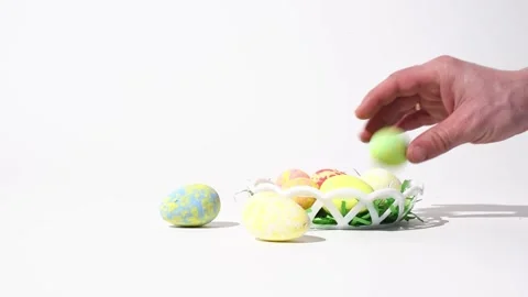 Easter decoration, close-up hand putting color eggs into basket on white Stock Footage 235812865